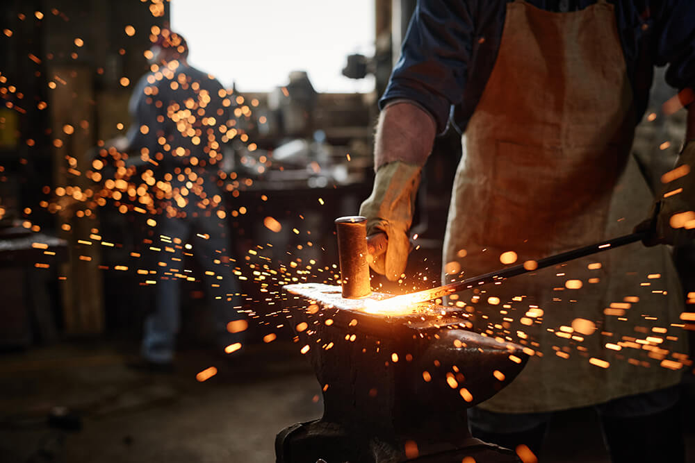 Close-up of blacksmith in apron working with hammer and iron in the workshop